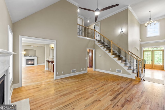 unfurnished living room with ceiling fan with notable chandelier, crown molding, high vaulted ceiling, and light hardwood / wood-style floors