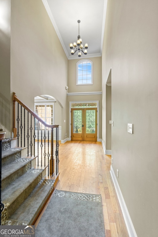 foyer entrance with crown molding, a towering ceiling, an inviting chandelier, and light hardwood / wood-style floors