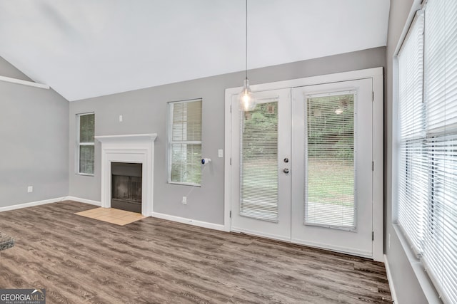 unfurnished living room with vaulted ceiling, a wealth of natural light, hardwood / wood-style flooring, and french doors