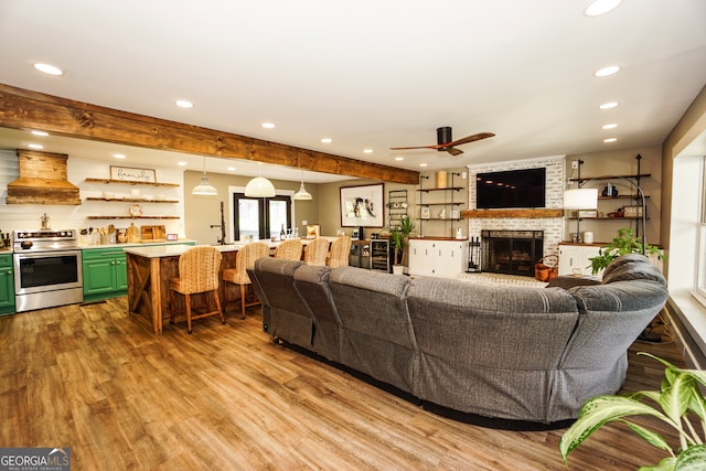 living room with ceiling fan, bar area, a large fireplace, and light hardwood / wood-style floors