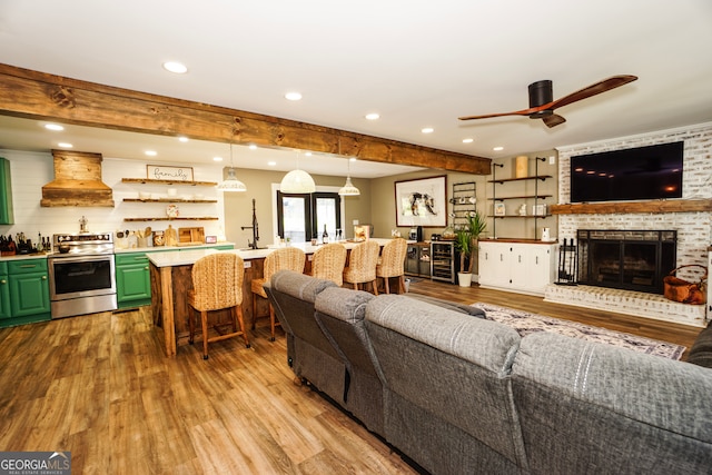 living room with light hardwood / wood-style flooring, ceiling fan, indoor bar, and a fireplace