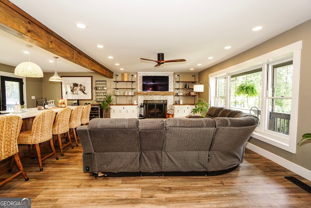 living room with ceiling fan, beamed ceiling, hardwood / wood-style flooring, and a fireplace