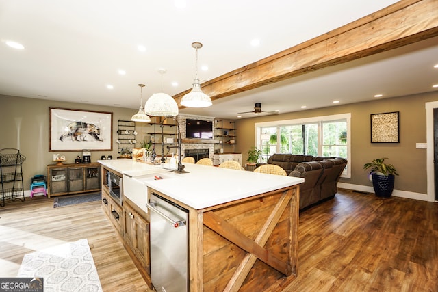 kitchen featuring stainless steel dishwasher, light hardwood / wood-style flooring, decorative light fixtures, a stone fireplace, and beam ceiling