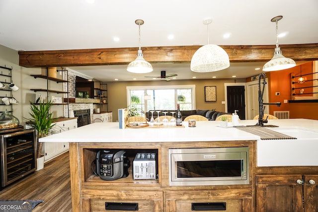 kitchen featuring dark hardwood / wood-style flooring, beverage cooler, a stone fireplace, beam ceiling, and stainless steel microwave