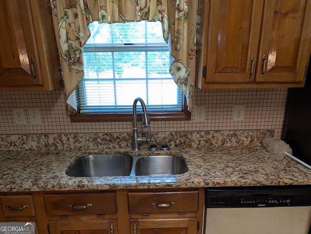 kitchen with light stone countertops, dishwasher, tasteful backsplash, and sink