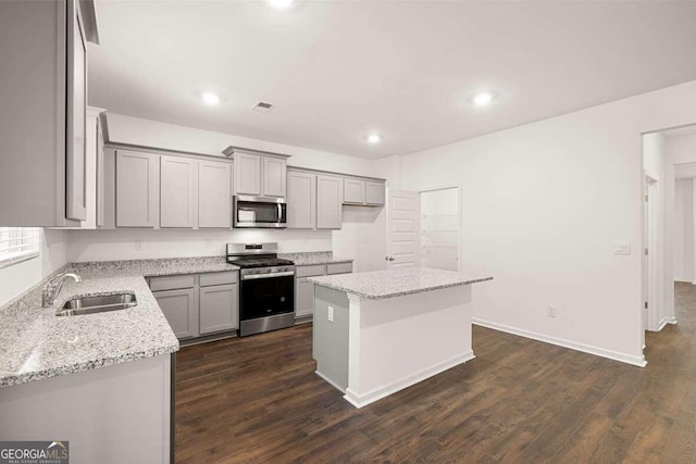 kitchen with dark wood-type flooring, sink, light stone counters, a center island, and stainless steel appliances