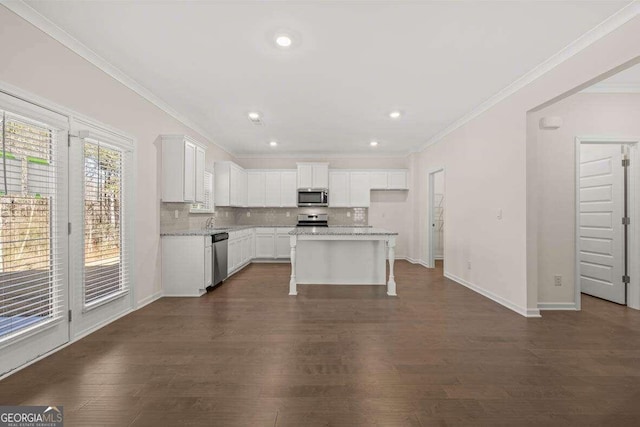 kitchen with dark wood-type flooring, appliances with stainless steel finishes, white cabinetry, tasteful backsplash, and a kitchen island