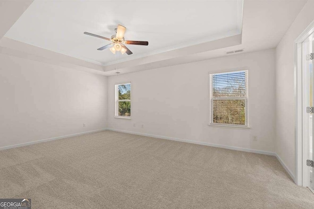 carpeted spare room with a healthy amount of sunlight, ceiling fan, and a tray ceiling