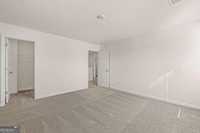 unfurnished bedroom featuring a walk in closet, light colored carpet, and a closet