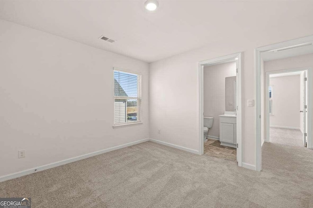 unfurnished bedroom featuring light colored carpet and connected bathroom