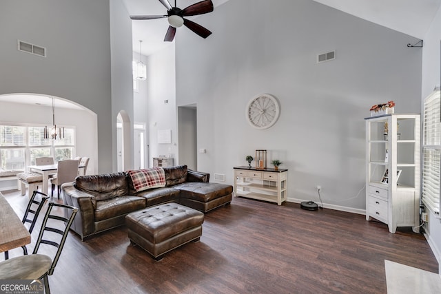 living room featuring ceiling fan with notable chandelier, dark wood-type flooring, and high vaulted ceiling