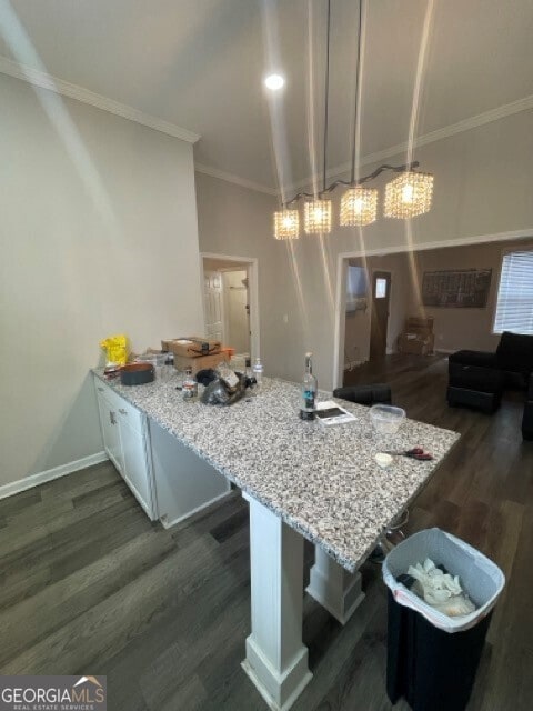 kitchen featuring ornamental molding, dark hardwood / wood-style flooring, light stone counters, hanging light fixtures, and a breakfast bar area