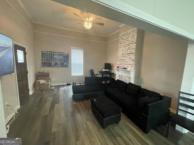 living room with a stone fireplace, ceiling fan, hardwood / wood-style flooring, and ornamental molding