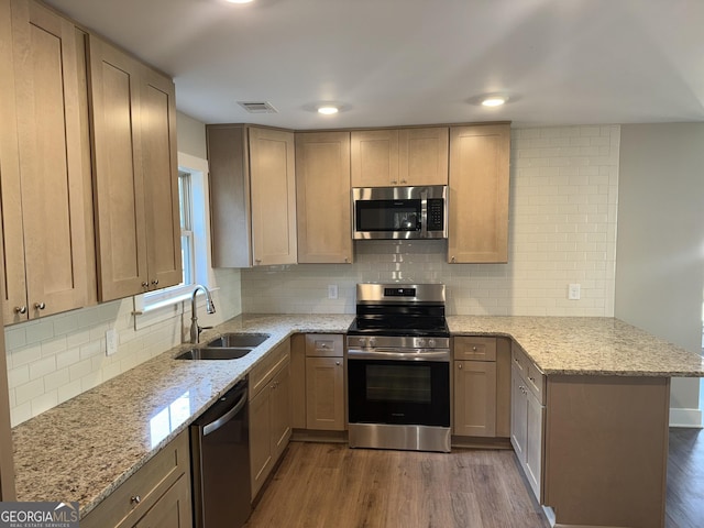 kitchen featuring light stone countertops, appliances with stainless steel finishes, a peninsula, wood finished floors, and a sink