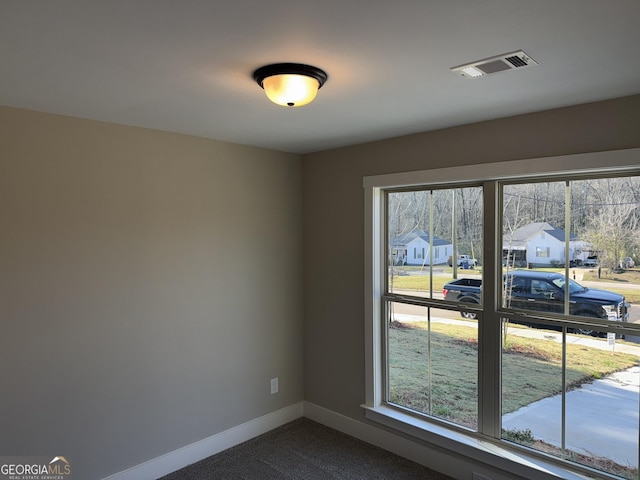 empty room with baseboards, visible vents, and dark colored carpet