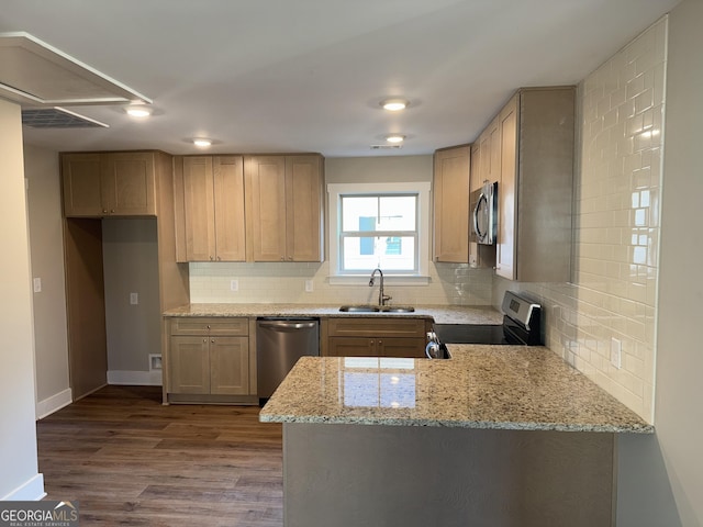 kitchen with light stone countertops, decorative backsplash, appliances with stainless steel finishes, wood finished floors, and a sink