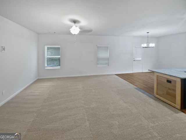 carpeted spare room featuring ceiling fan with notable chandelier