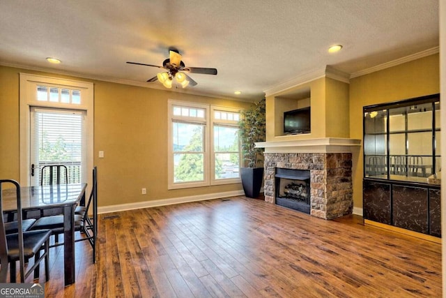 living room featuring a textured ceiling, a fireplace, crown molding, hardwood / wood-style flooring, and ceiling fan