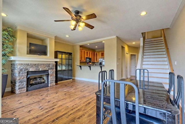 dining room featuring crown molding, light hardwood / wood-style flooring, ceiling fan, and a fireplace