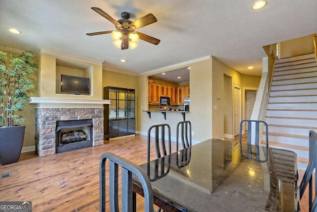 dining space featuring light hardwood / wood-style floors, ceiling fan, ornamental molding, and a fireplace