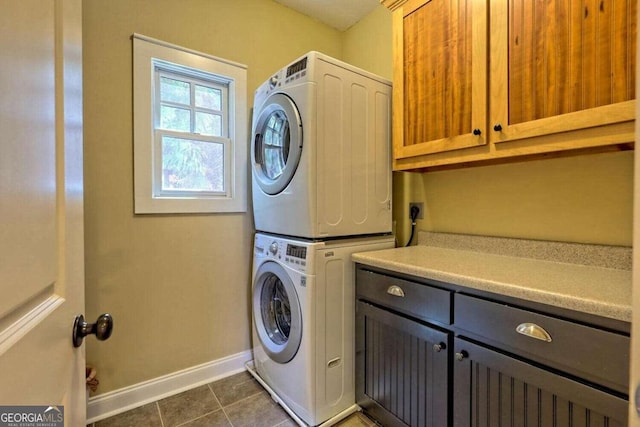 laundry room featuring dark tile patterned floors, cabinets, and stacked washer / drying machine