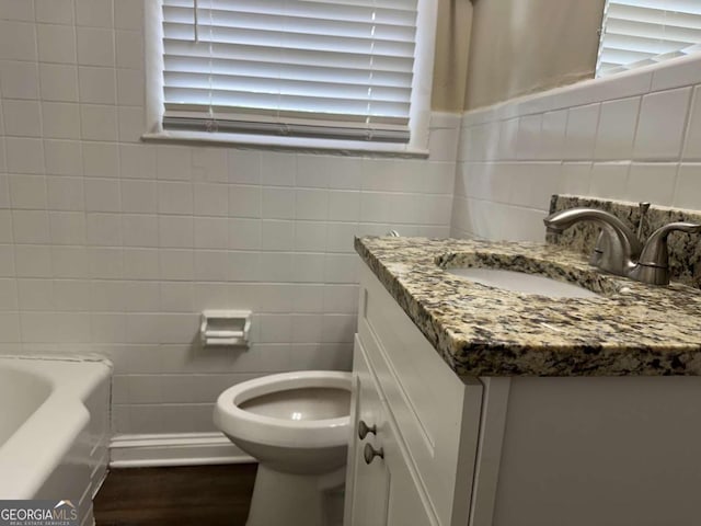 bathroom featuring hardwood / wood-style floors, toilet, a bath, tile walls, and vanity