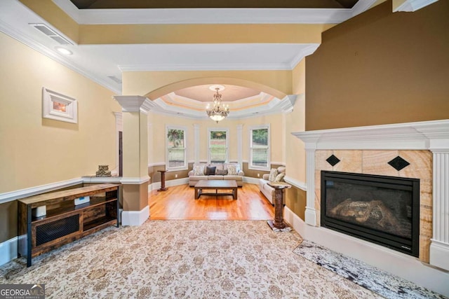 living room with hardwood / wood-style flooring, an inviting chandelier, a raised ceiling, ornamental molding, and ornate columns