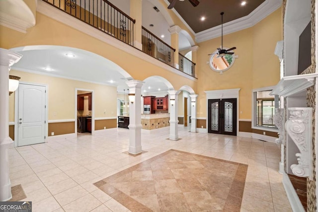 foyer entrance featuring ornamental molding, a towering ceiling, ceiling fan, and ornate columns