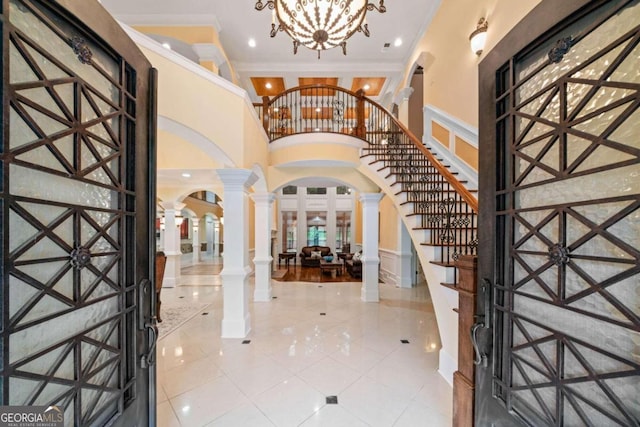 foyer entrance with crown molding, decorative columns, an inviting chandelier, and tile patterned floors