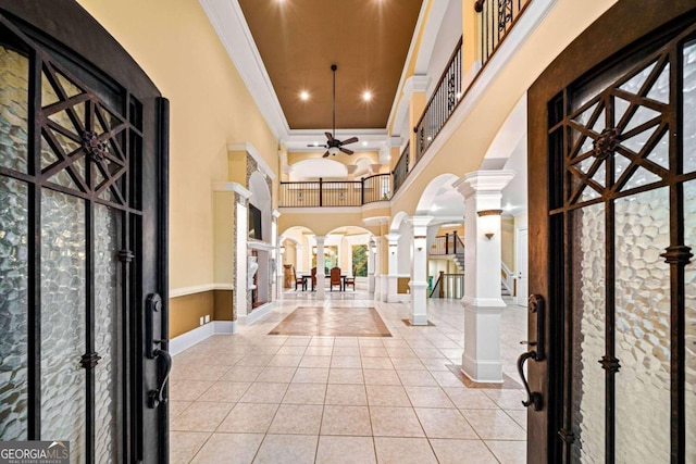 tiled foyer with a high ceiling, ceiling fan, crown molding, and ornate columns