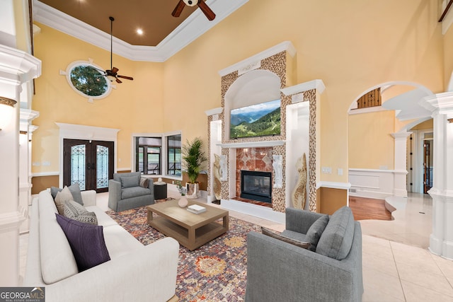 tiled living room with ceiling fan, a towering ceiling, and a tiled fireplace