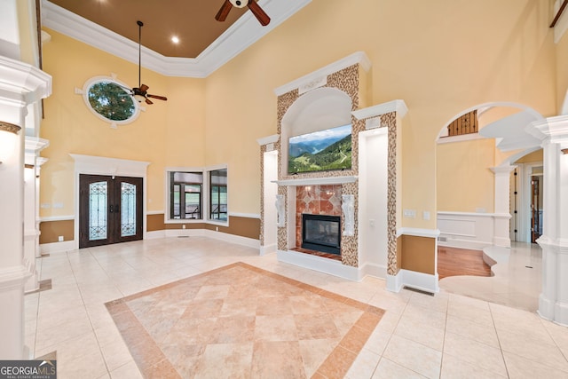 unfurnished living room featuring a tile fireplace, decorative columns, crown molding, a high ceiling, and ceiling fan