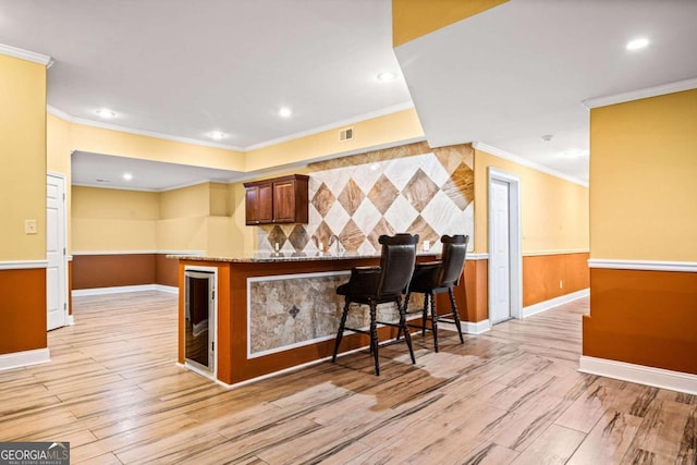 kitchen with a breakfast bar, light wood-type flooring, kitchen peninsula, crown molding, and light stone countertops