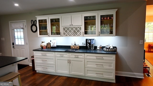 bar featuring dark wood-type flooring, white cabinets, and a healthy amount of sunlight