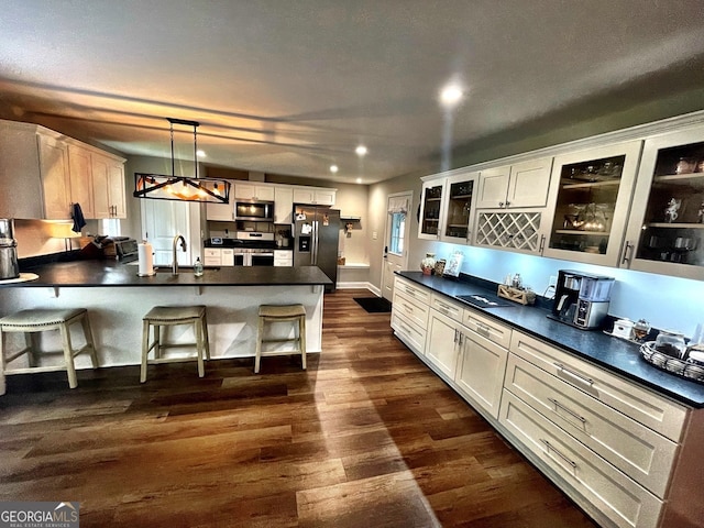 kitchen featuring a kitchen island with sink, hanging light fixtures, dark wood-type flooring, a breakfast bar, and appliances with stainless steel finishes