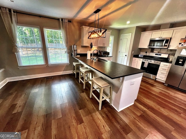 kitchen featuring stainless steel appliances, white cabinetry, dark hardwood / wood-style floors, pendant lighting, and a kitchen bar