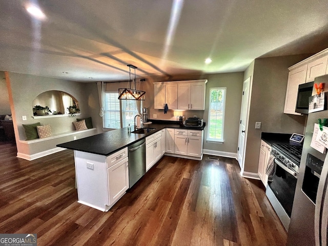 kitchen with decorative light fixtures, appliances with stainless steel finishes, dark wood-type flooring, kitchen peninsula, and white cabinets