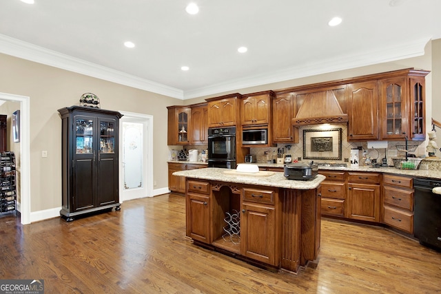 kitchen featuring backsplash, hardwood / wood-style floors, black appliances, a kitchen island, and custom range hood