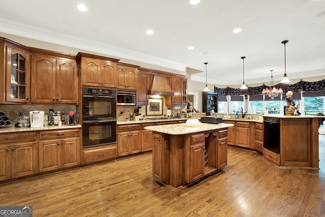 kitchen with black appliances, a kitchen island, wood-type flooring, hanging light fixtures, and custom range hood