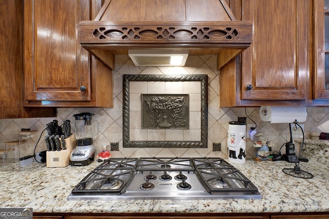 kitchen with light stone countertops, backsplash, stainless steel gas stovetop, and custom range hood