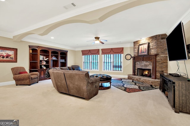 carpeted living room featuring ceiling fan, ornamental molding, and a stone fireplace