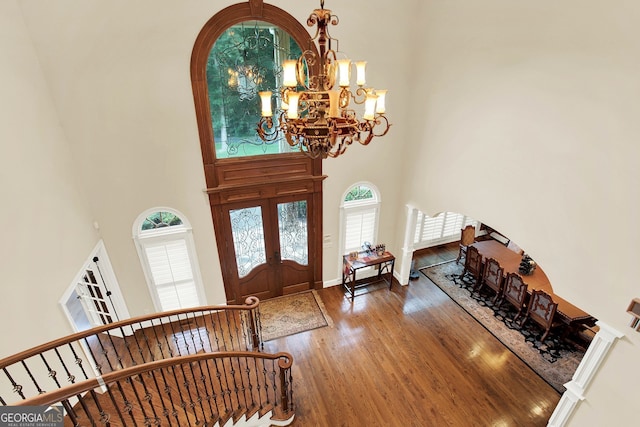 entryway featuring french doors, a towering ceiling, a chandelier, and wood-type flooring