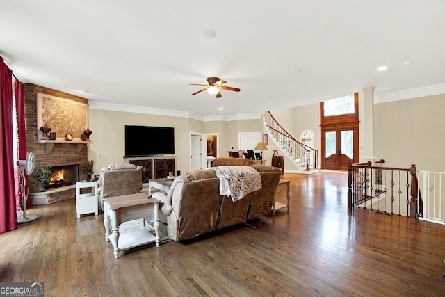 living room with ceiling fan, dark hardwood / wood-style floors, crown molding, and a stone fireplace