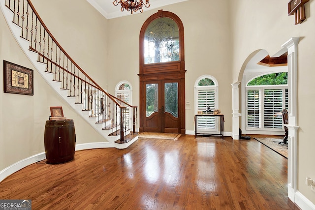 foyer with a towering ceiling, french doors, an inviting chandelier, hardwood / wood-style flooring, and decorative columns