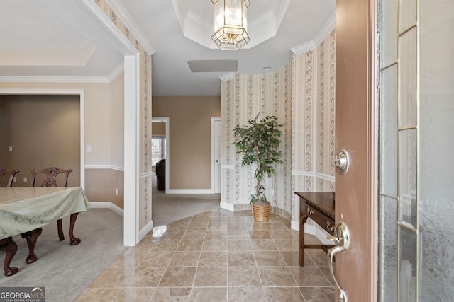 carpeted entrance foyer with a tray ceiling, ornamental molding, and an inviting chandelier