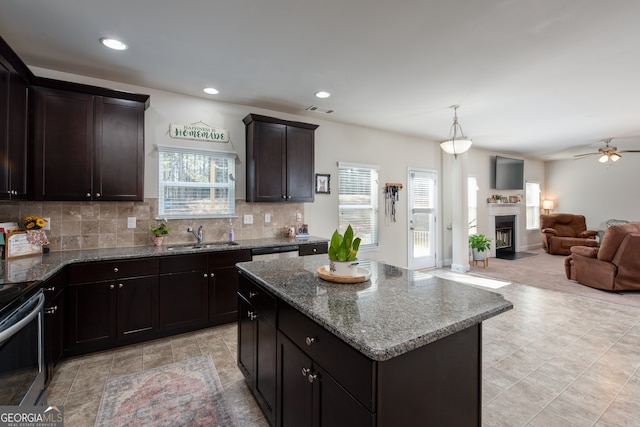 kitchen featuring a kitchen island, dark brown cabinets, decorative backsplash, ceiling fan, and light stone counters