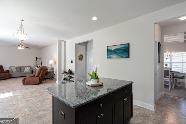 kitchen with ceiling fan with notable chandelier, light stone counters, a kitchen island, and hanging light fixtures