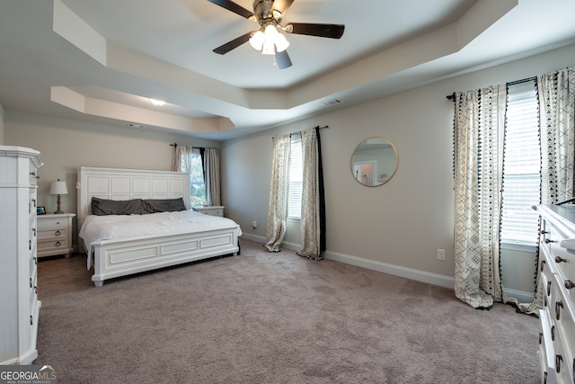 carpeted bedroom with ceiling fan and a raised ceiling