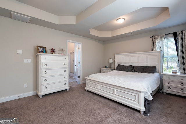 bedroom featuring dark carpet, a tray ceiling, and connected bathroom