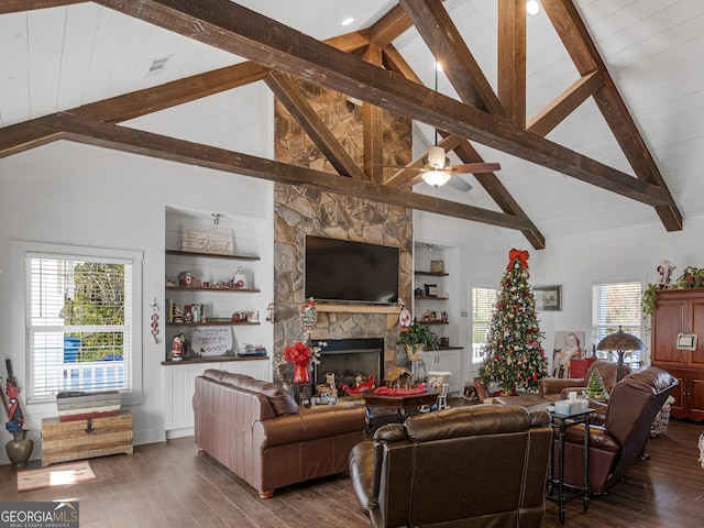 living room with beamed ceiling, dark hardwood / wood-style flooring, a stone fireplace, high vaulted ceiling, and ceiling fan